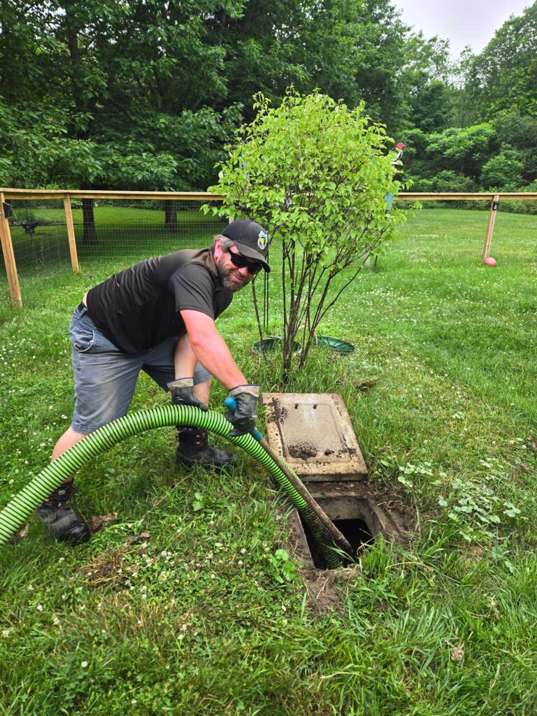 picture of a man holding a pump out hose inside of a septic tank